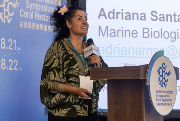 Adriana at a presentation dias with slide on screen.