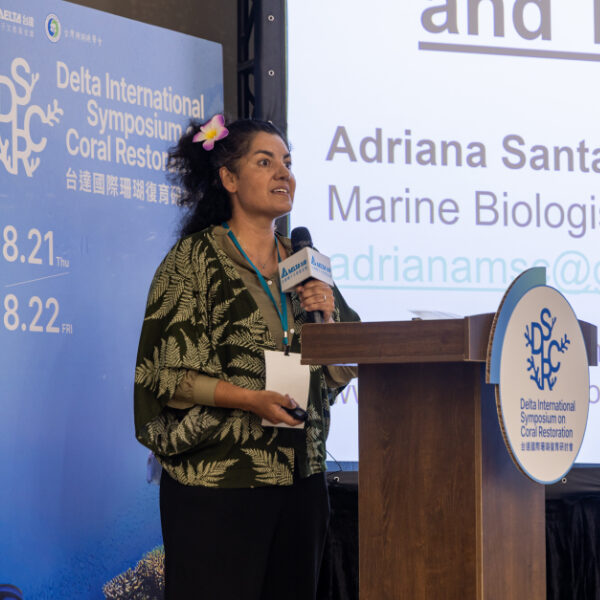 Adriana at a presentation dias with slide on screen.