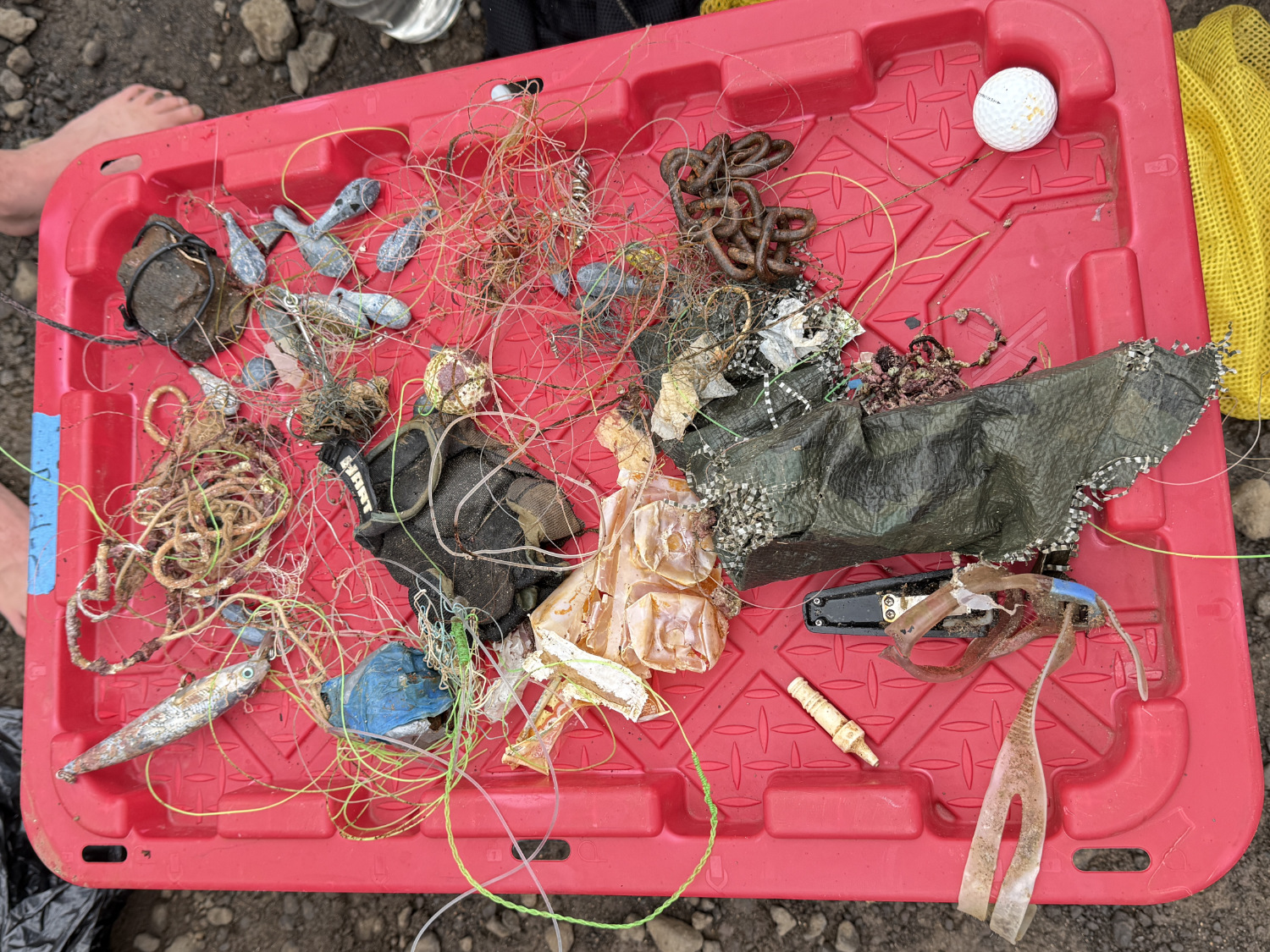 A large red tray containing debris from the ocean including fishing line, lead weights, a fish-shaped lure, chain, anod other trash.
